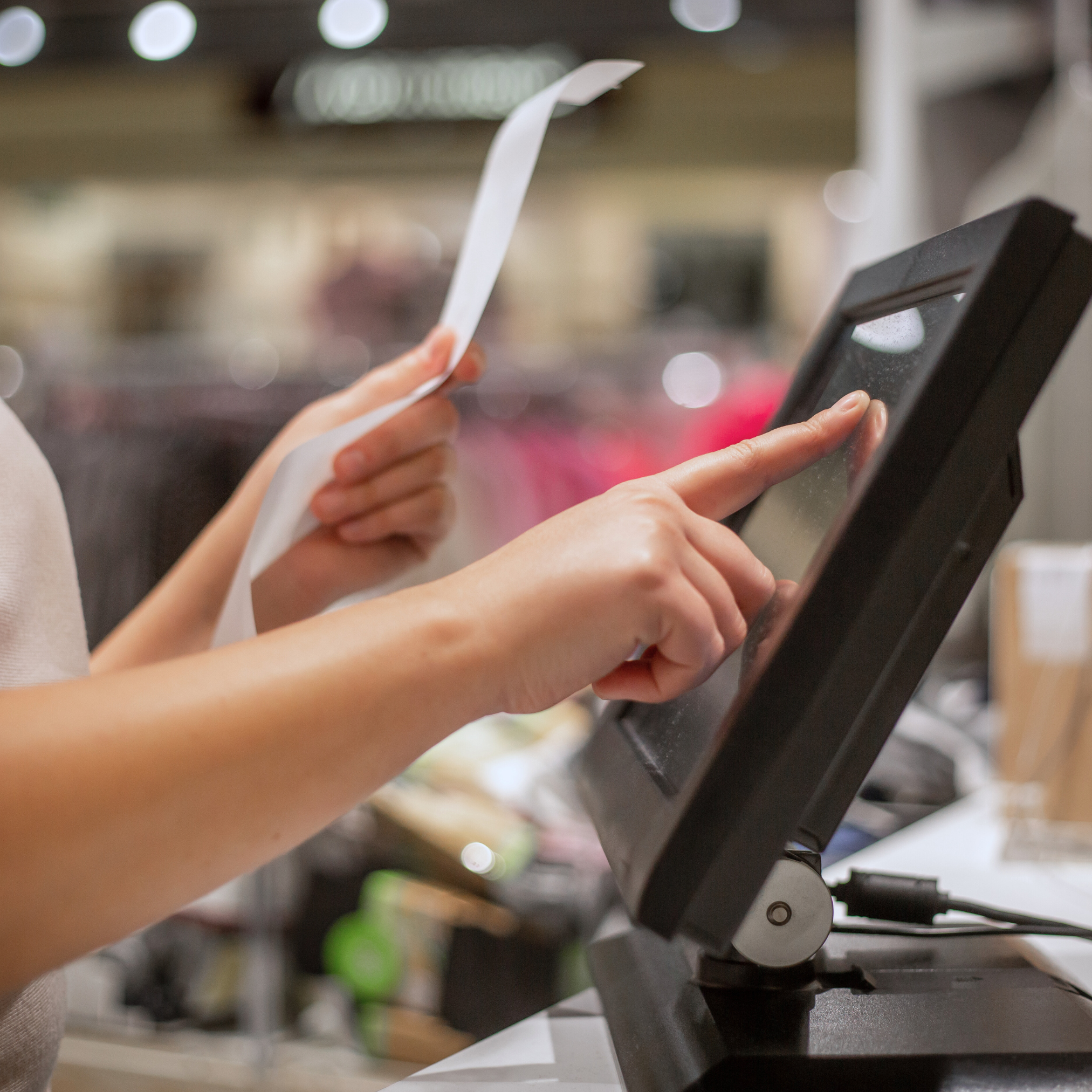 Person holding a receipt and using a touchscreen point-of-sale terminal in a retail store environment.
