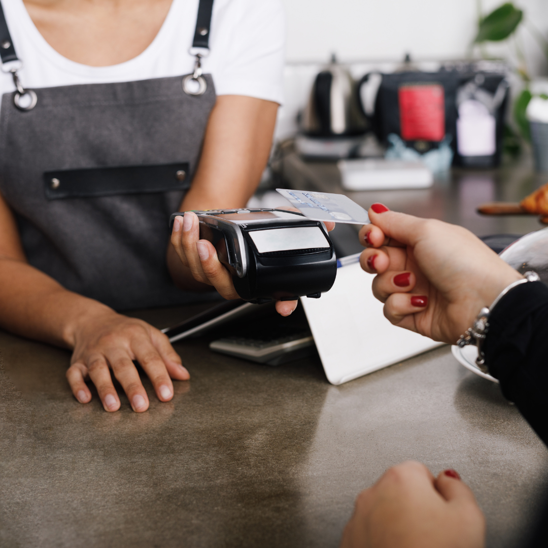 Person makes a contactless payment with a card at a counter as a cashier holds the payment terminal.